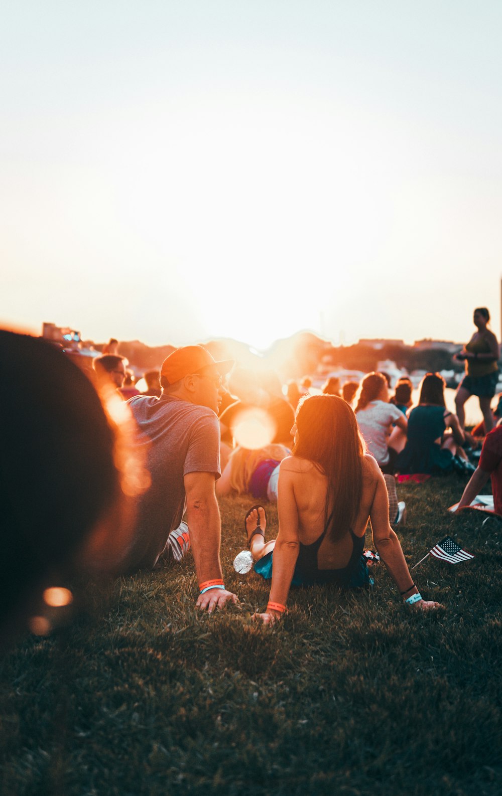 man and woman sitting on grass surrounded with people during golden hour