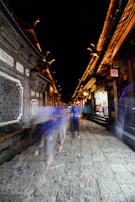 Street scene showing blurred figures walking past ancient stone buildings.