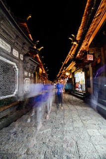 Street scene showing blurred figures walking past ancient stone buildings.