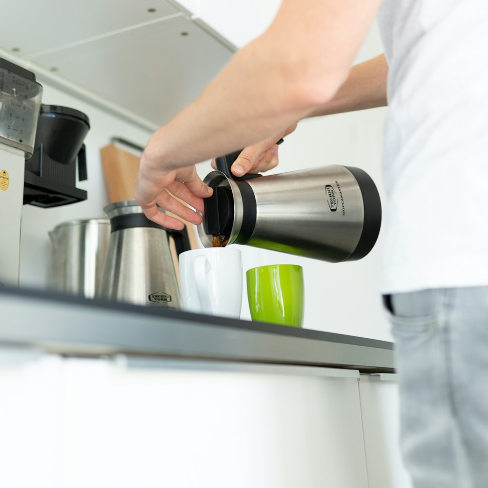 Person mit Wasserkocher gießt Kaffee in die Tasse
