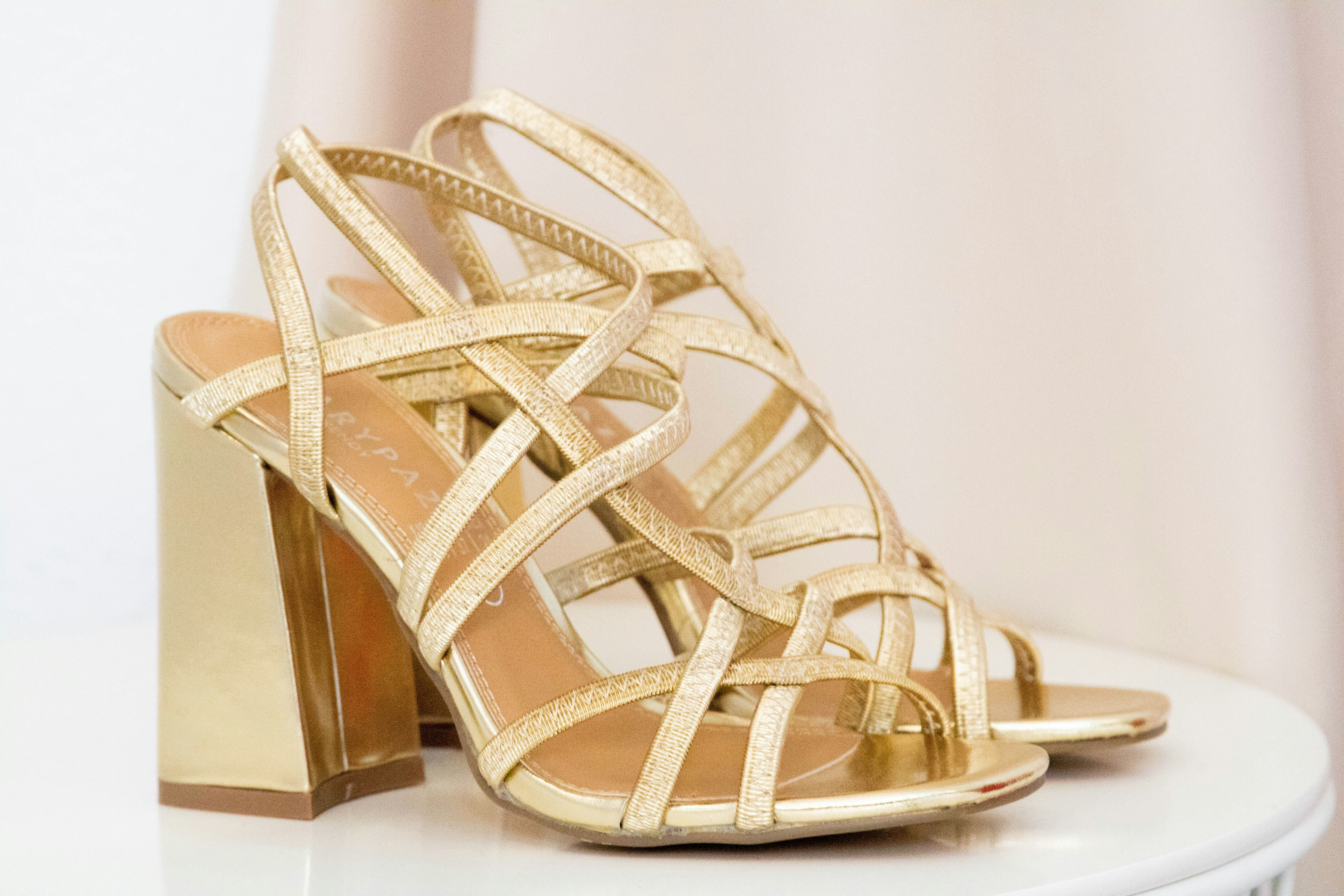 Strappy gold sandals on warm sand, summer fashion lifestyle photography