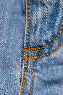Close-up of blue denim fabric with detailed orange stitching along a seam.