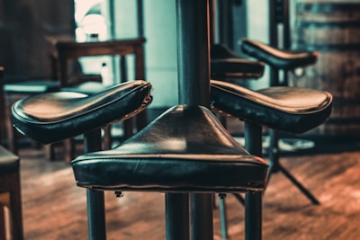 A close-up of a high stool with leather upholstery and sturdy legs.