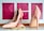 A pair of glossy, pink high-heeled shoes is displayed on a white surface. In front of the shoes, there is a strand of cream-colored pearls partially wrapped around a small pink fabric accessory. The background consists of three pink rectangles featuring floral patterns.