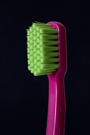A close-up of a toothbrush with bright green bristles and a pink handle against a dark background.