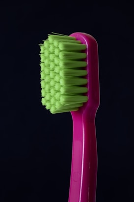 A close-up of a toothbrush with bright green bristles and a pink handle against a dark background.