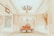 A luxurious interior setting featuring an ornate chandelier hanging from a high ceiling, with elegant architectural details such as decorative columns and arches. The center of the image has a vintage-style, red upholstered settee placed on an intricate patterned carpet.