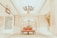 A luxurious interior setting featuring an ornate chandelier hanging from a high ceiling, with elegant architectural details such as decorative columns and arches. The center of the image has a vintage-style, red upholstered settee placed on an intricate patterned carpet.