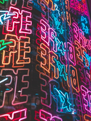 A variety of neon signs in different sizes and colors hanging on a dark wall