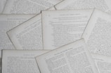 Several sheets of paper with printed text are scattered and overlapping. The text appears to be related to educational topics, with headings like 'Natural and Common Objects' and 'Free-Arm and Industrial Drawing.' The pages are arranged casually, creating a layered effect.
