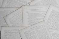Several sheets of paper with printed text are scattered and overlapping. The text appears to be related to educational topics, with headings like 'Natural and Common Objects' and 'Free-Arm and Industrial Drawing.' The pages are arranged casually, creating a layered effect.