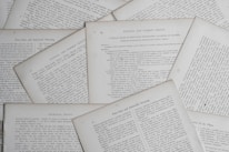 Several sheets of paper with printed text are scattered and overlapping. The text appears to be related to educational topics, with headings like 'Natural and Common Objects' and 'Free-Arm and Industrial Drawing.' The pages are arranged casually, creating a layered effect.