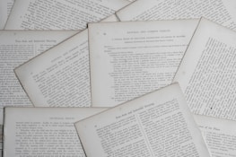 Several sheets of paper with printed text are scattered and overlapping. The text appears to be related to educational topics, with headings like 'Natural and Common Objects' and 'Free-Arm and Industrial Drawing.' The pages are arranged casually, creating a layered effect.