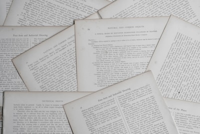 Several sheets of paper with printed text are scattered and overlapping. The text appears to be related to educational topics, with headings like 'Natural and Common Objects' and 'Free-Arm and Industrial Drawing.' The pages are arranged casually, creating a layered effect.