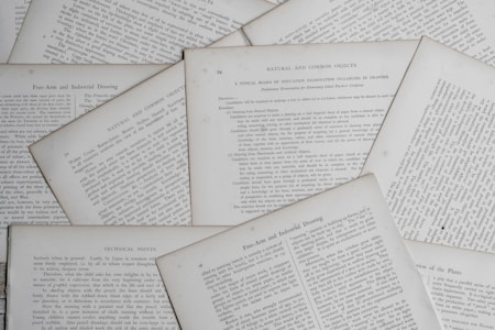 Several sheets of paper with printed text are scattered and overlapping. The text appears to be related to educational topics, with headings like 'Natural and Common Objects' and 'Free-Arm and Industrial Drawing.' The pages are arranged casually, creating a layered effect.