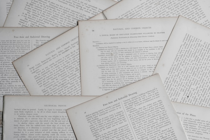Several sheets of paper with printed text are scattered and overlapping. The text appears to be related to educational topics, with headings like 'Natural and Common Objects' and 'Free-Arm and Industrial Drawing.' The pages are arranged casually, creating a layered effect.