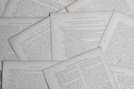 Several sheets of paper with printed text are scattered and overlapping. The text appears to be related to educational topics, with headings like 'Natural and Common Objects' and 'Free-Arm and Industrial Drawing.' The pages are arranged casually, creating a layered effect.
