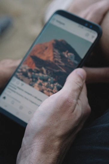 A happy traveler using a smartphone app to book a flight and rent a car with scenic mountains in the background.