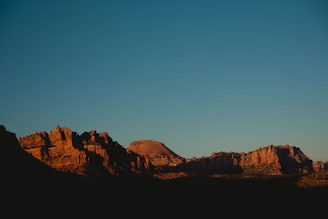 A rugged mountain range under a fiery sunset sky, with a lone horse rider silhouetted against the horizon.