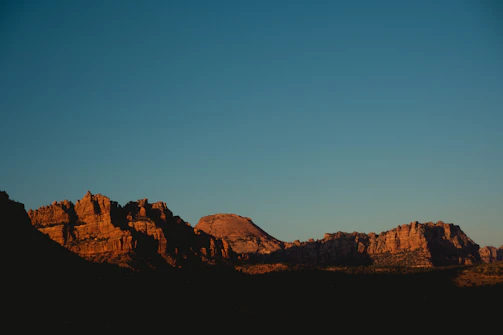 A rugged mountain range under a fiery sunset sky, with a lone horse rider silhouetted against the horizon.