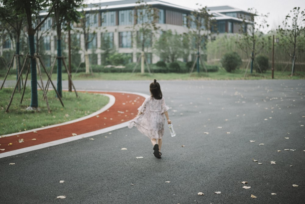 girl holding clear plastic bottle walking on road