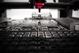 A machine is assembling or inspecting a circuit board. Various electronic components are visible, and the process seems to be automated with precision equipment.