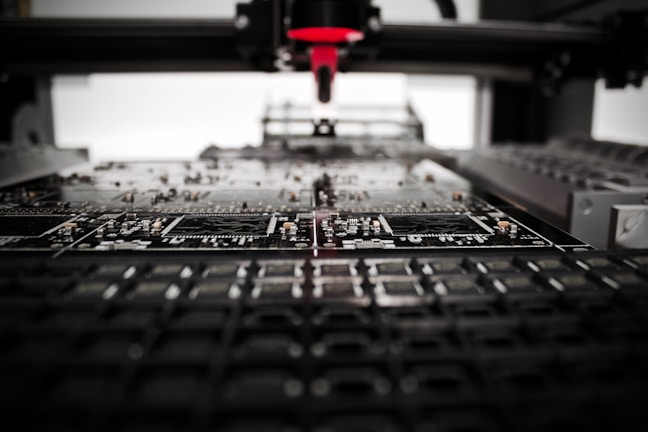 A machine is assembling or inspecting a circuit board. Various electronic components are visible, and the process seems to be automated with precision equipment.