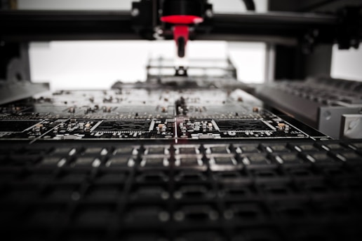 A machine is assembling or inspecting a circuit board. Various electronic components are visible, and the process seems to be automated with precision equipment.