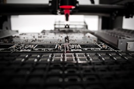 A machine is assembling or inspecting a circuit board. Various electronic components are visible, and the process seems to be automated with precision equipment.