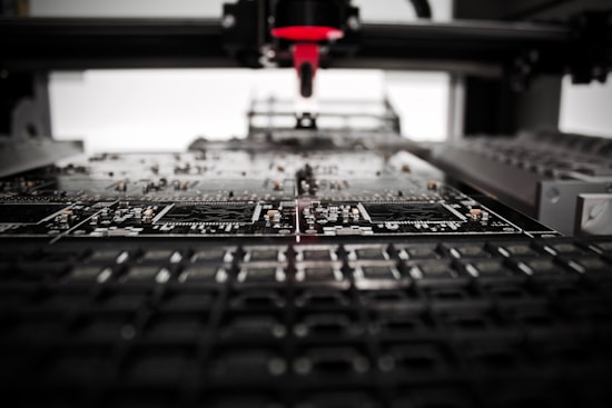 A machine is assembling or inspecting a circuit board. Various electronic components are visible, and the process seems to be automated with precision equipment.