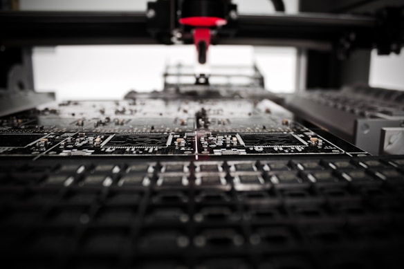 A machine is assembling or inspecting a circuit board. Various electronic components are visible, and the process seems to be automated with precision equipment.