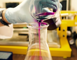 person pouring purple liquid on clear glass container