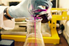 person pouring purple liquid on clear glass container