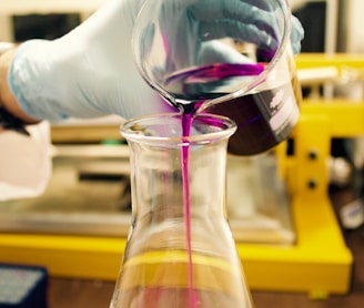 person pouring purple liquid on clear glass container