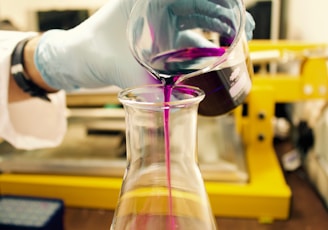 person pouring purple liquid on clear glass container