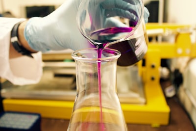 person pouring purple liquid on clear glass container chemistry teams background