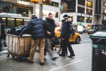 man walking on street beside man pushing cart
