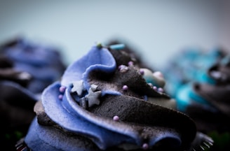 A close-up of a beautifully decorated black and gold cupcake with intricate icing swirls.
