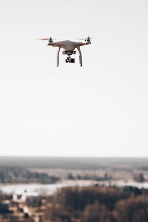 A drone capturing aerial topographic mapping over a sprawling construction site under clear skies.