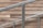 A staircase railing composed of silver metal bars is positioned diagonally against a backdrop of wood paneling. The wood panels have a rustic, natural appearance with various shades of brown, adding a warm contrast to the cool tone of the metal.