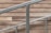 A staircase railing composed of silver metal bars is positioned diagonally against a backdrop of wood paneling. The wood panels have a rustic, natural appearance with various shades of brown, adding a warm contrast to the cool tone of the metal.