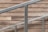 A staircase railing composed of silver metal bars is positioned diagonally against a backdrop of wood paneling. The wood panels have a rustic, natural appearance with various shades of brown, adding a warm contrast to the cool tone of the metal.