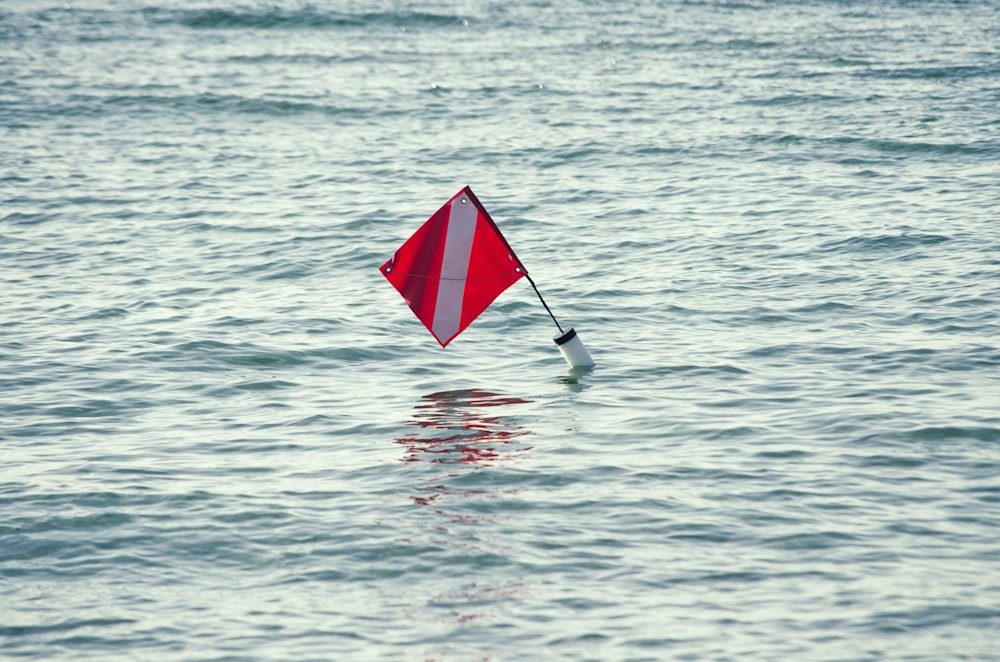 a red and white kite floating on top of a body of water