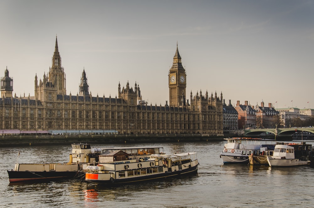 vier weiße Boote, die auf dem Fluss neben Big Ben in London unterwegs sind