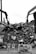 Two large industrial machines with claws are moving a pile of metal scraps and debris. In the foreground, several signs say 'STOP' and 'DO NOT ENTER'. The machinery is surrounded by heaps of twisted metal and broken materials.