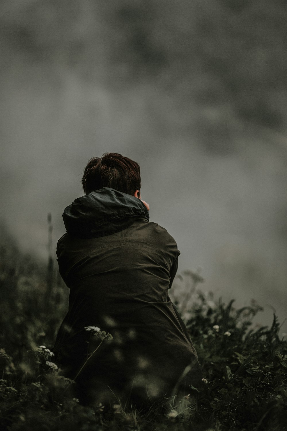 selective focus photo of person in black hooded jacket sitting on green grass field at daytime