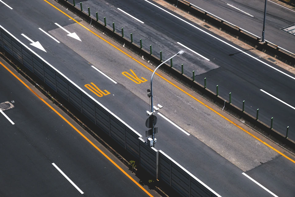 Two-lane highway with white dividing line and yellow stripe, surrounded by green poles and street