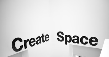 Black bold text reading 'Create Space' is displayed on a white wall, likely in a modern interior setting. The wall and text create a minimalist and artistic visual impression.