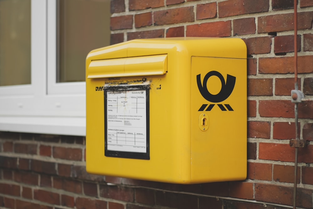 yellow mailbox on brown wall bricks