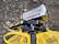 A black Panasonic Full HD camcorder is mounted on a tripod. It has various features labeled on it, including 72x zoom and 10.0 Mega Pixels. The camcorder is positioned above a yellow fabric or bag on a ground covered with dry leaves.